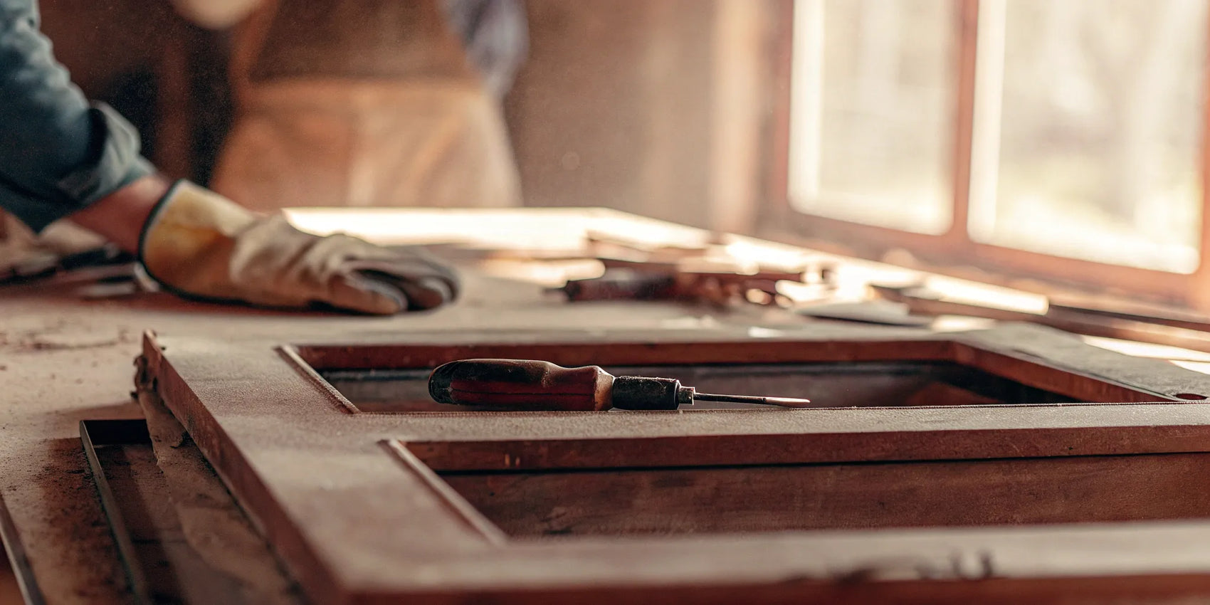 A person with gloves uses a screwdriver to replace the glass in a wood stove door.