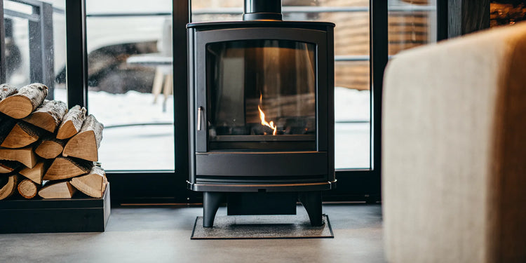 A modern hybrid catalytic wood stove burning efficiently, with a stack of firewood nearby.